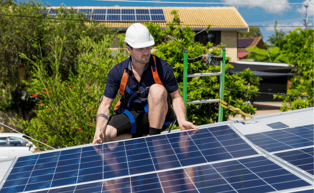 Technik v ochranném postroji kontroluje solární panely na střeše domu.